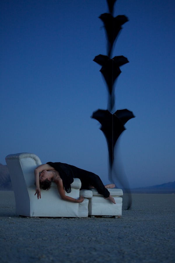 Ruth Whiting reclined in a chair in the Black Rock Desert with a stack of 5 black Flowx silk kites by Tim Elverston